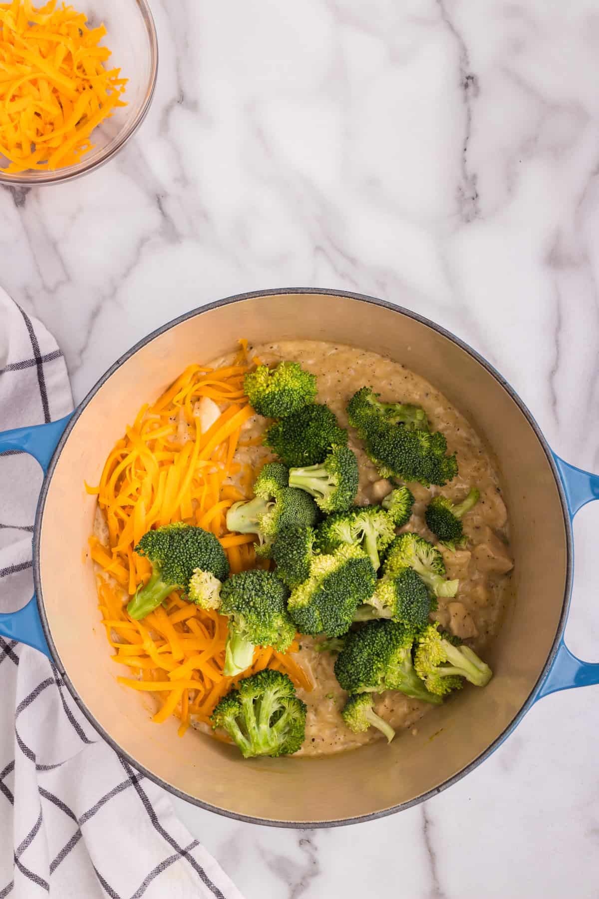 Dutch oven with cheesy chicken broccoli and rice casserole ingredients in it not fully cooked.