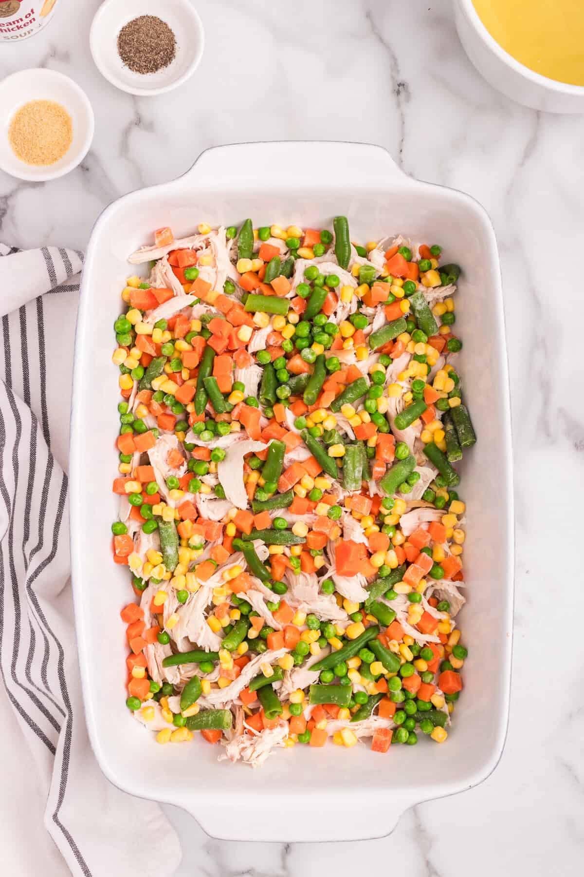 Overhead picture of white baking dish with mixed vegetables layered on top of chicken.