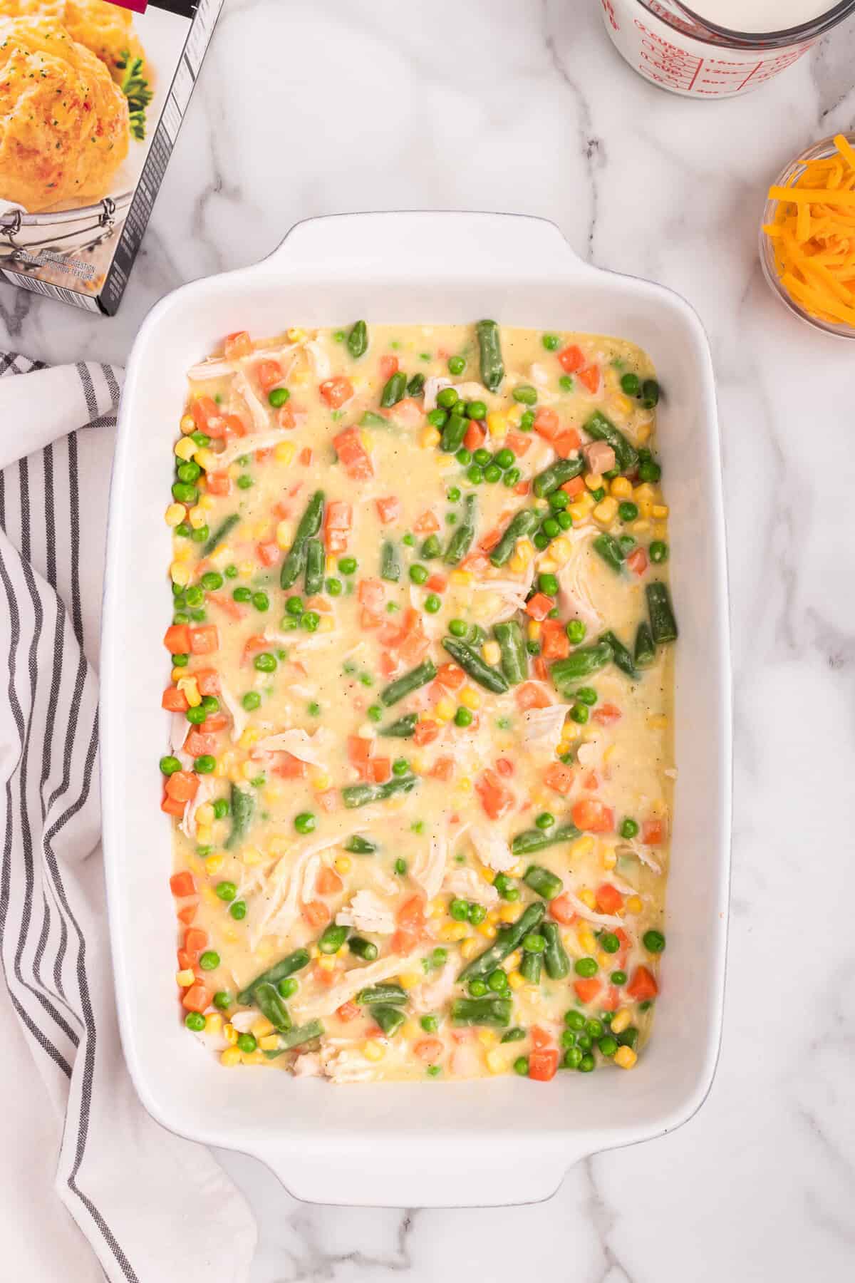 Overhead picture of white baking dish with partial chicken cobbler ingredients.