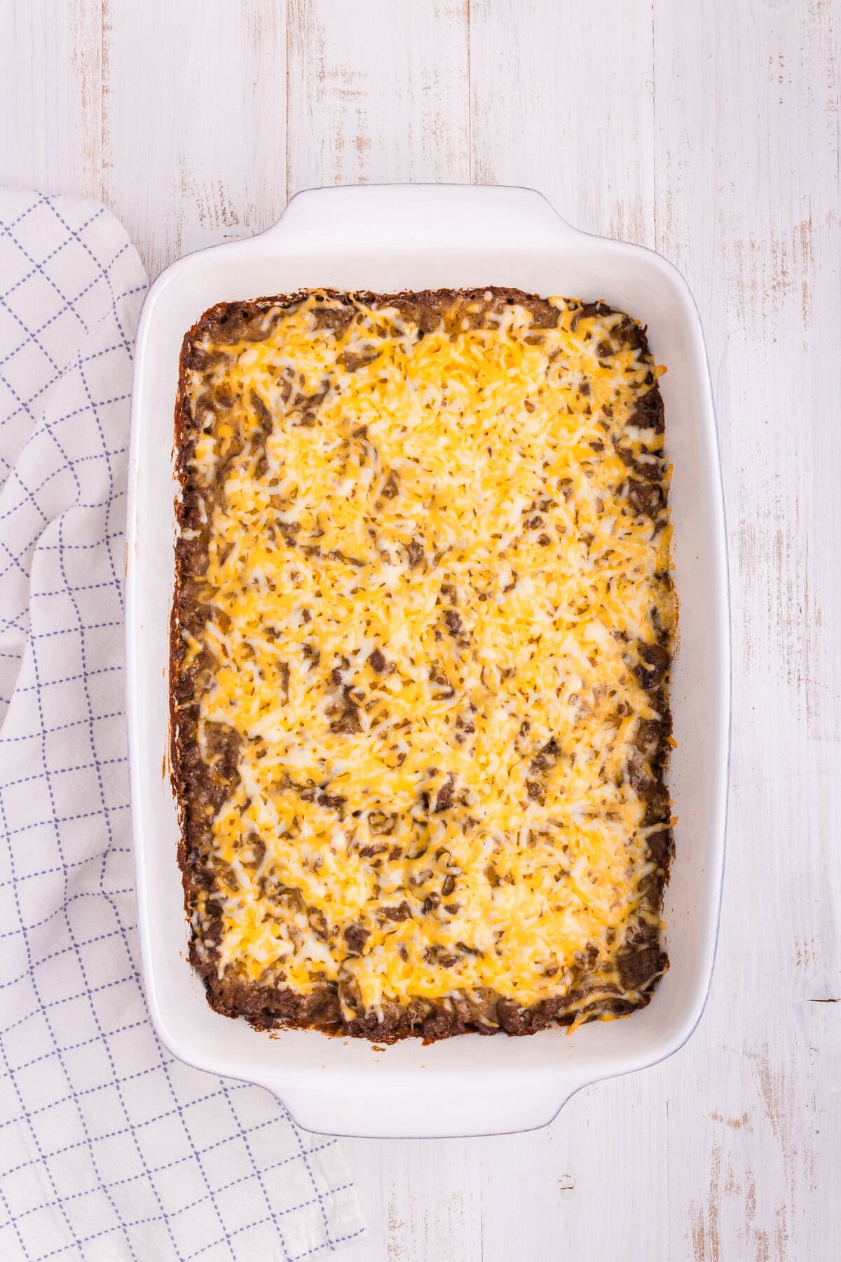 Overhead picture of white pan with ground beef and potato casserole ingredients in it.