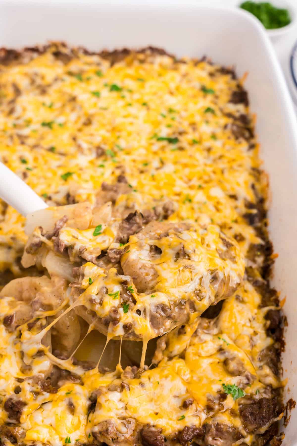 Close up of white serving spoon scooping cooked ground beef and potato casserole in it.