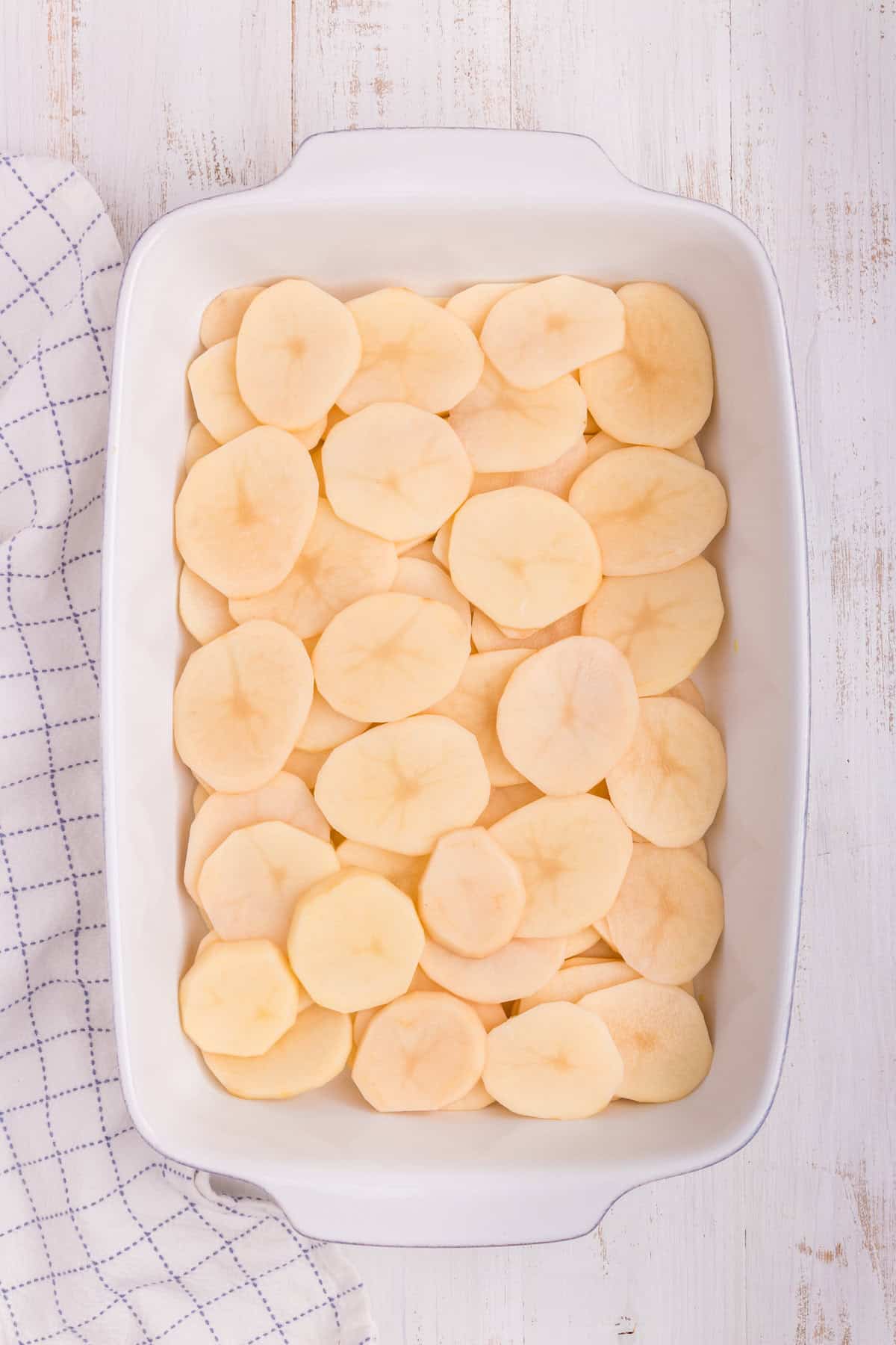 White pan with sliced potatoes layered at the bottom