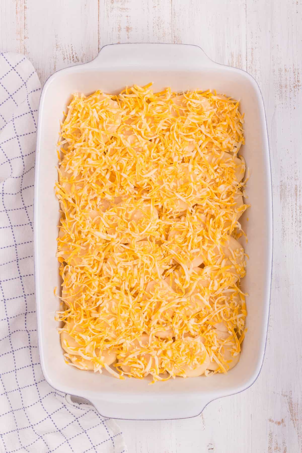 Overhead picture of white pan with shredded cheese and potatoes in it.