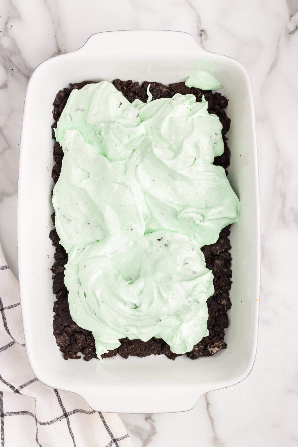 White pan with crush oreos layered with mint ice cream spread on top