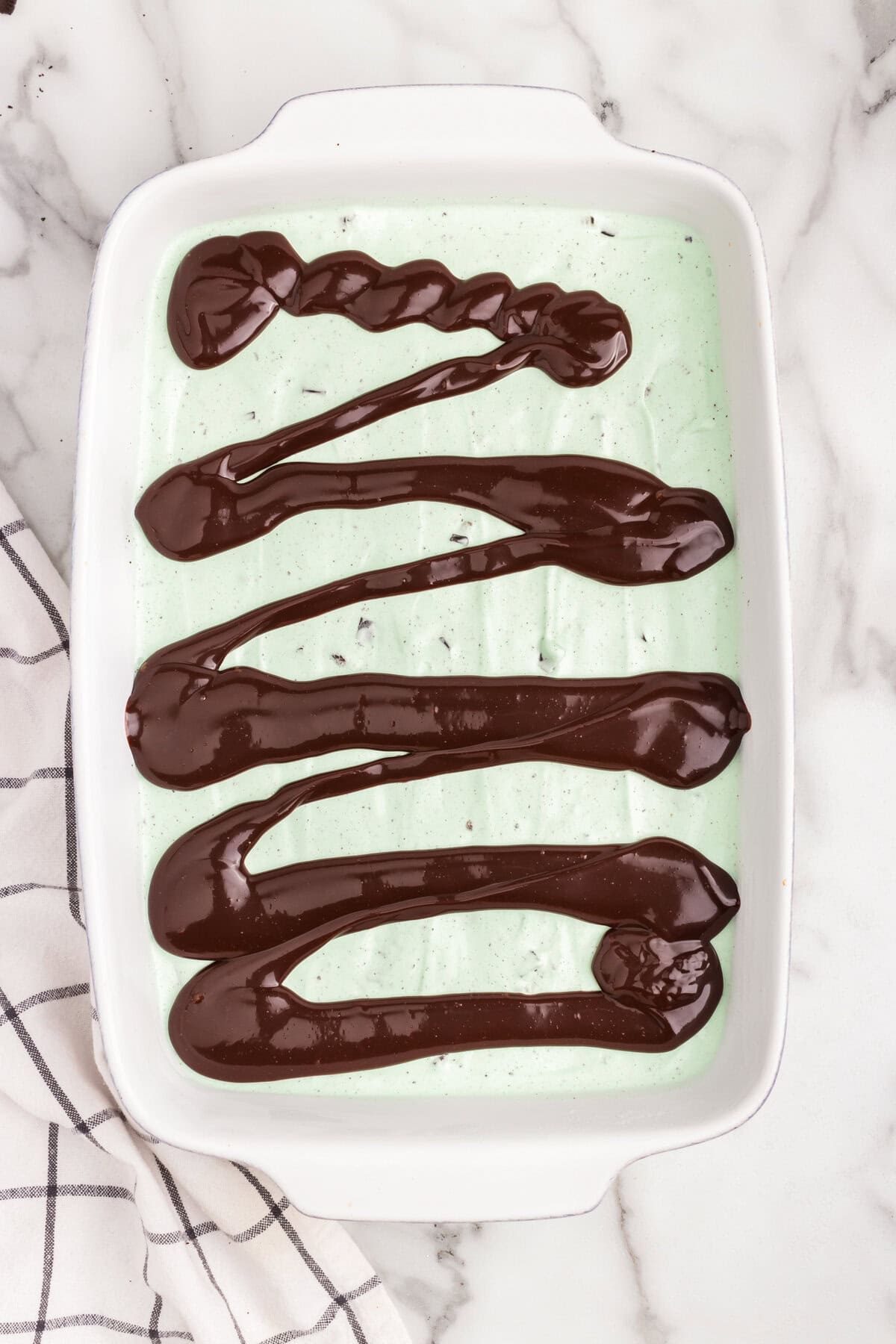 White pan with mint ice cream spread out with hot fudge sauce drizzled across