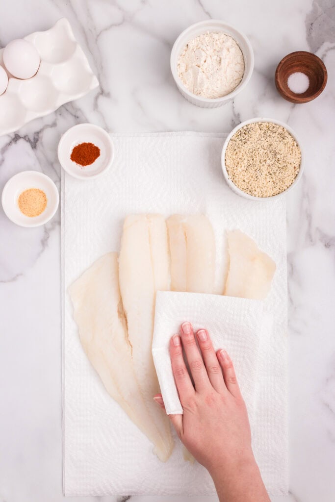Overhead picture of cutting board with fish and hand pat drying fish with a paper towel
