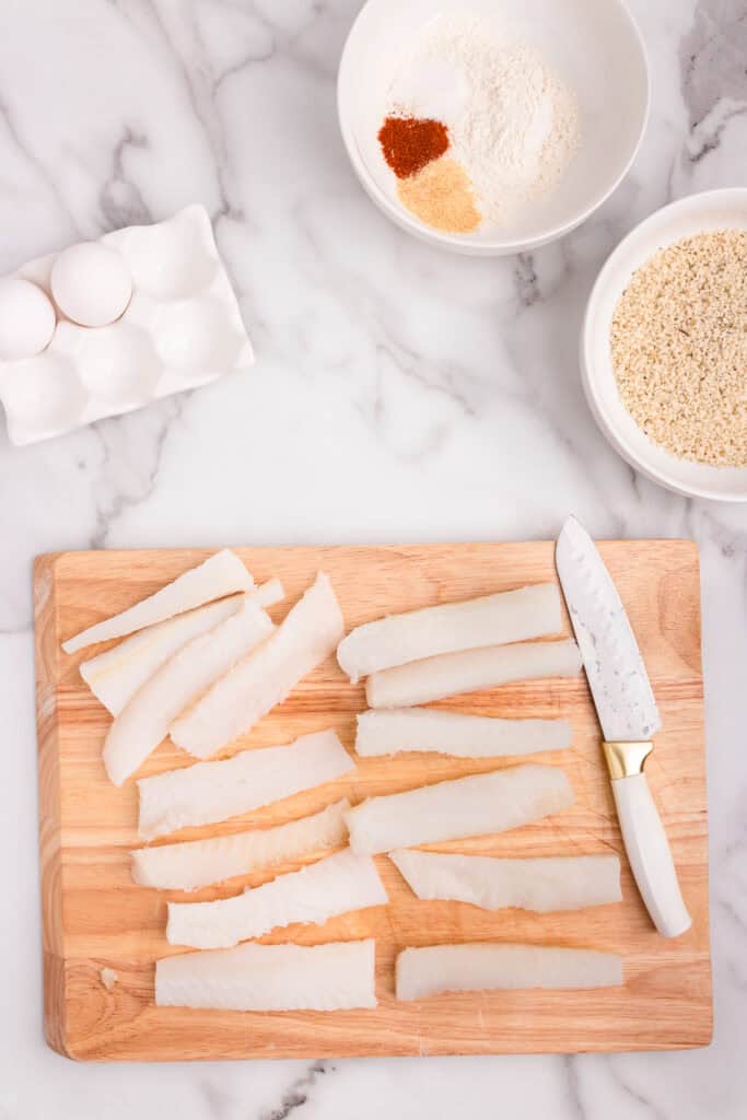 Overhead picture of cutting board with fish and knife on it and other ingredients in bowls around it.