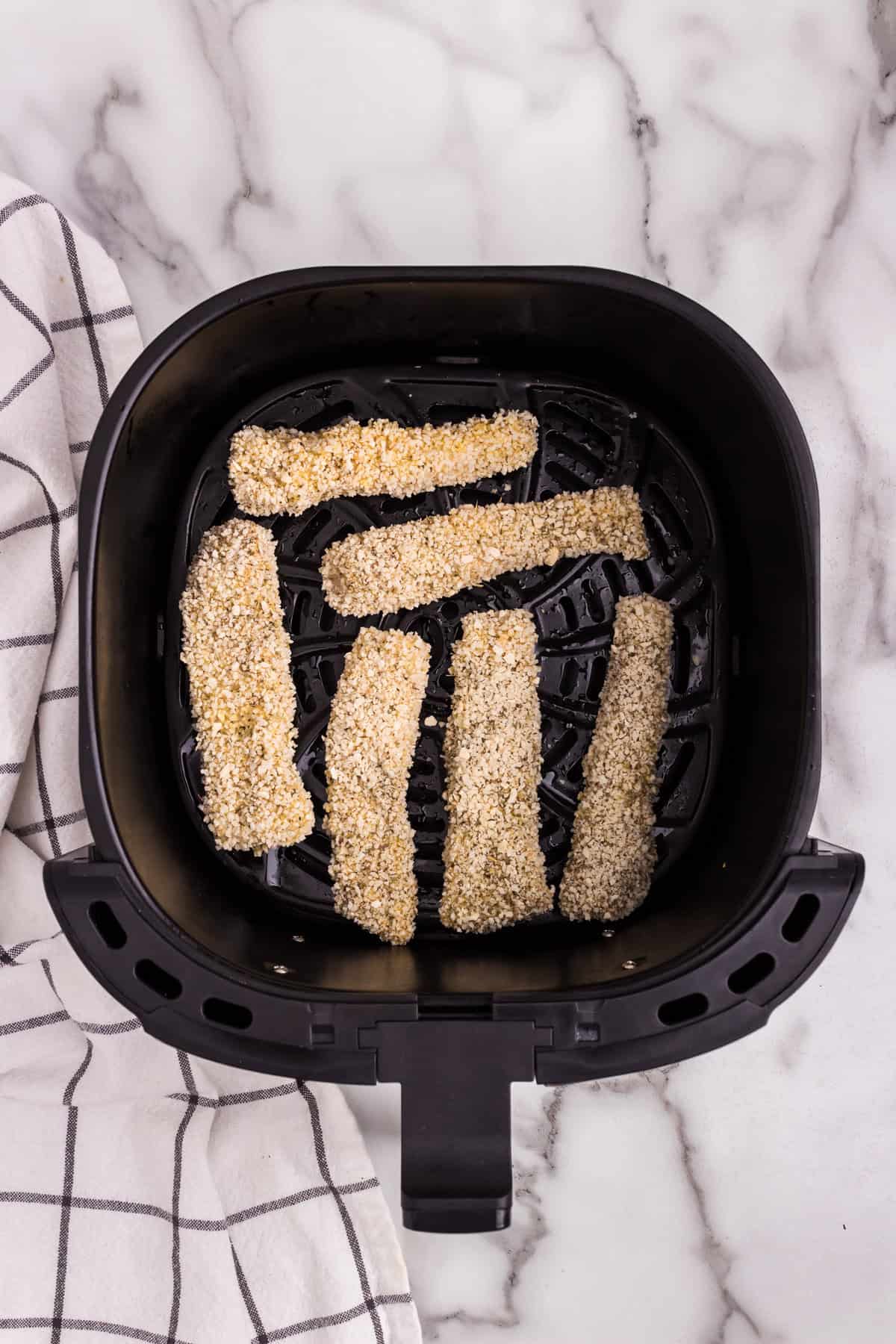 Overhead picture of air fryer basket with uncooked fish sticks in it.