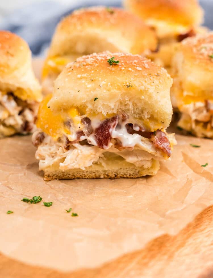 Wooden cutting board with chicken bacon ranch sliders on it.