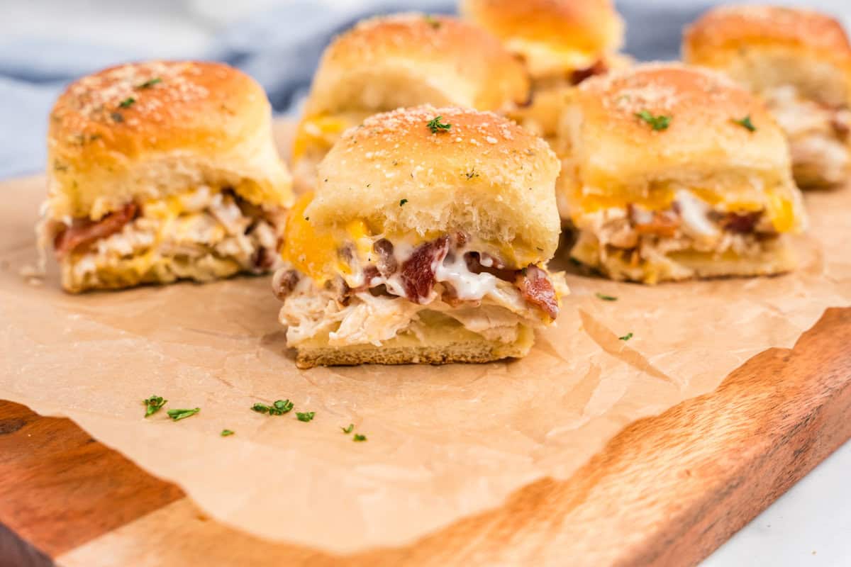 Wooden cutting board with chicken bacon ranch sliders on it.