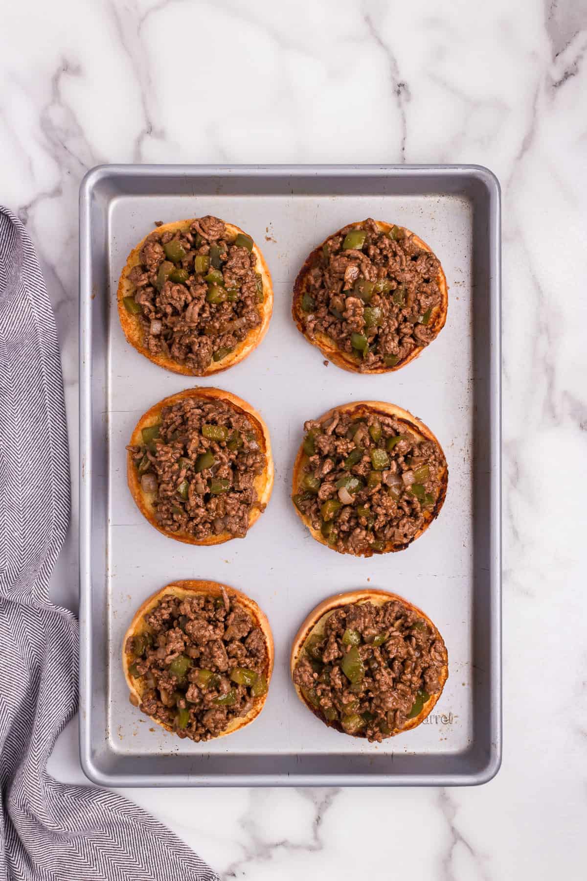 Overhead picture of metal baking sheet with 6 buns with Philly Cheesesteak meat on them.