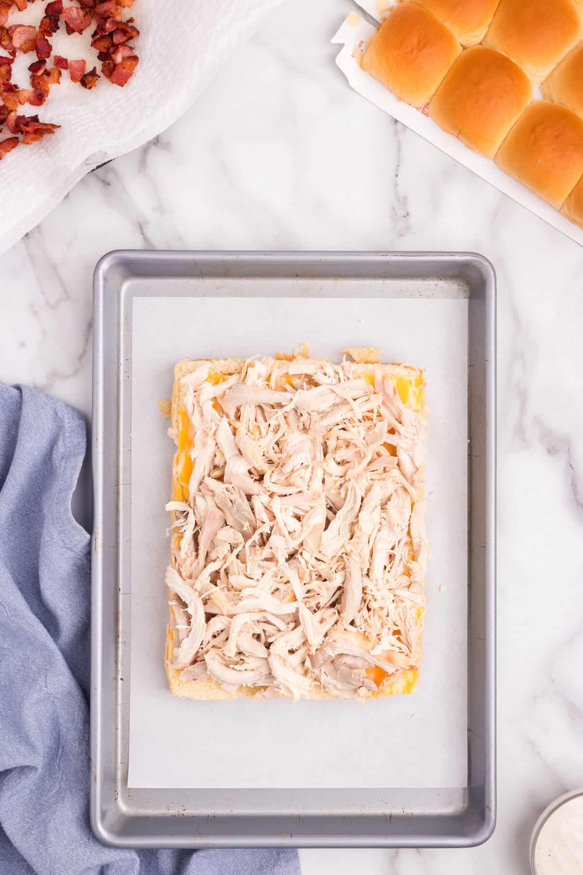 Overhead picture of shredded chicken layered on Hawaiian buns.