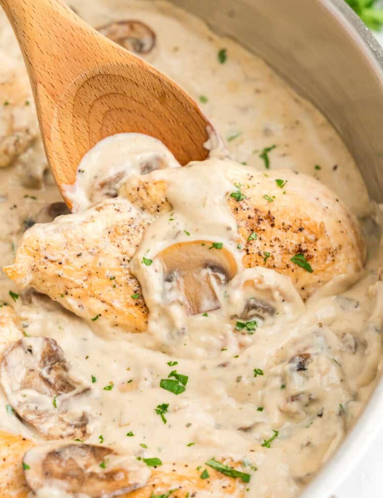 Using a wooden spoon to stir Skillet Cream of Mushroom Chicken in stovetop skillet