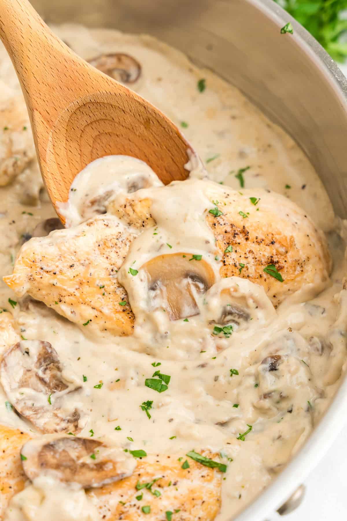 Using a wooden spoon to stir Skillet Cream of Mushroom Chicken in stovetop skillet