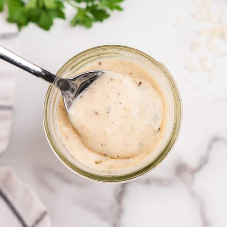 Glass jar filled with sauce and metal spoon scooping out sauce