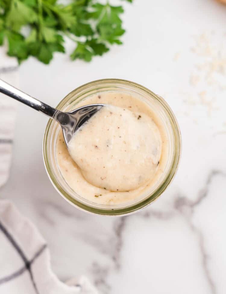 Glass jar filled with sauce and metal spoon scooping out sauce