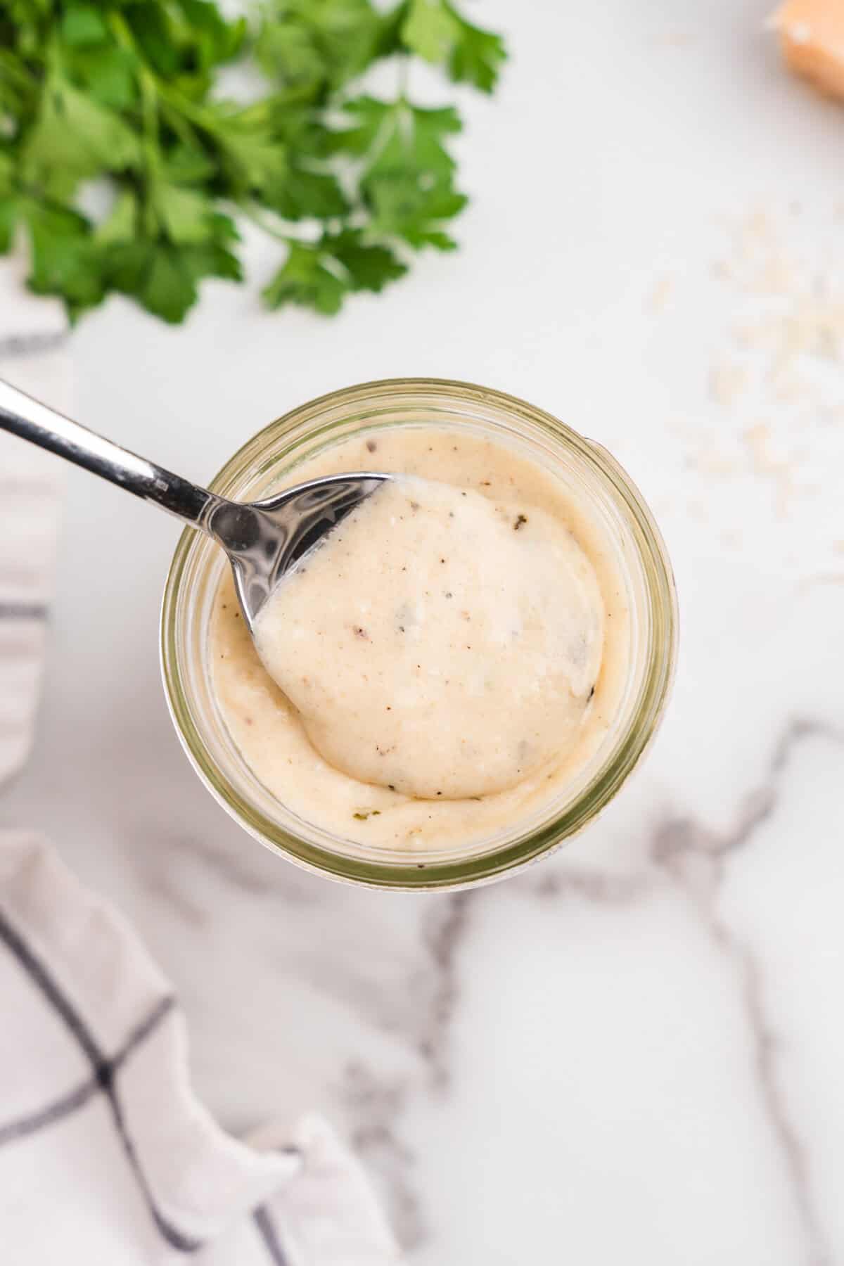 Glass jar filled with sauce and metal spoon scooping out sauce