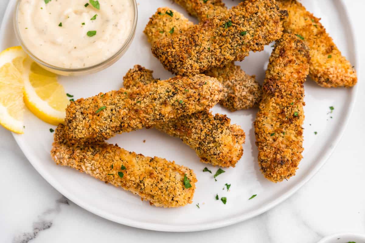 Overhead picture of white plate with air fryer fish sticks and dipping sauce on it.