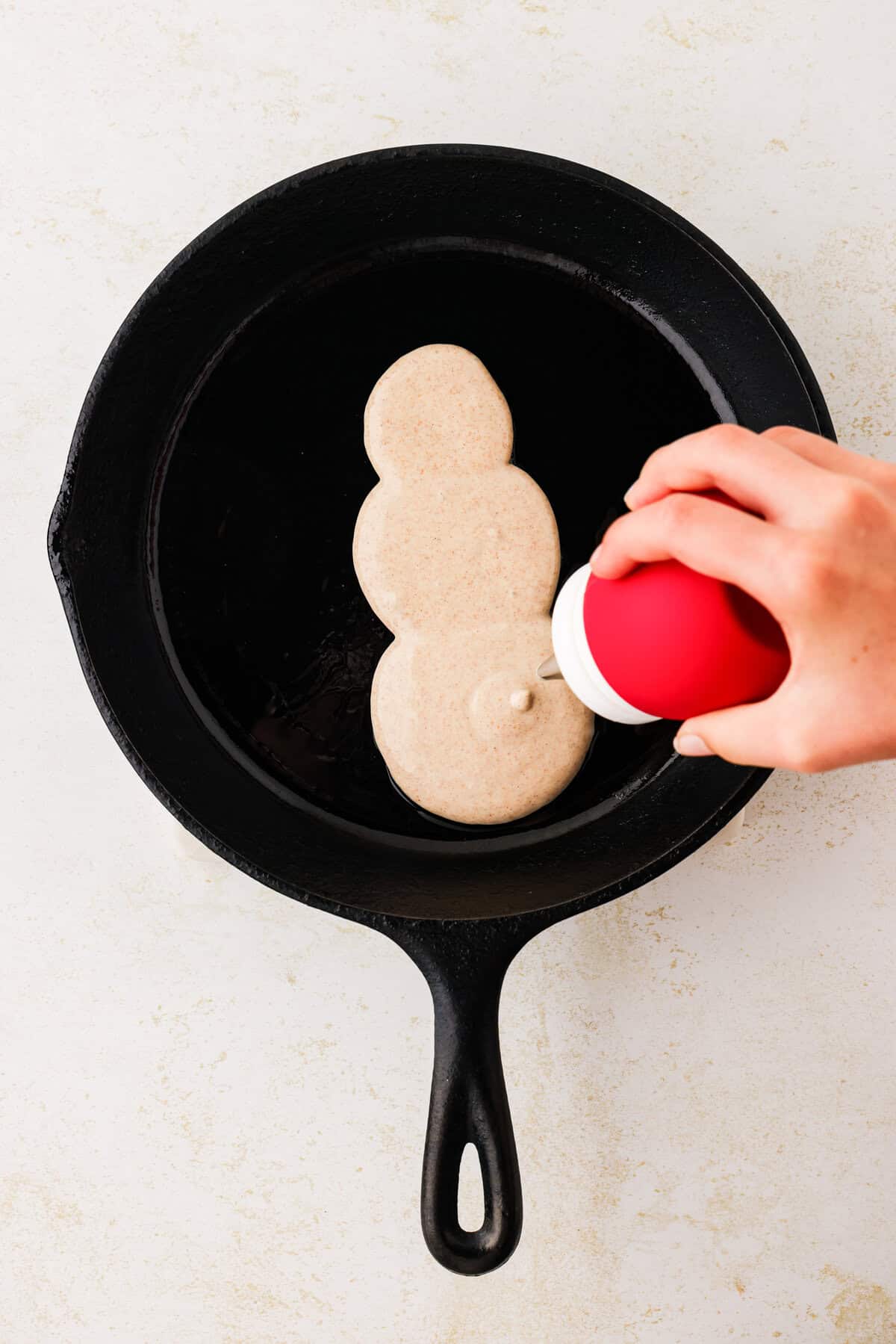 Hand squeezing frosting bulb to make snowmans bottom.