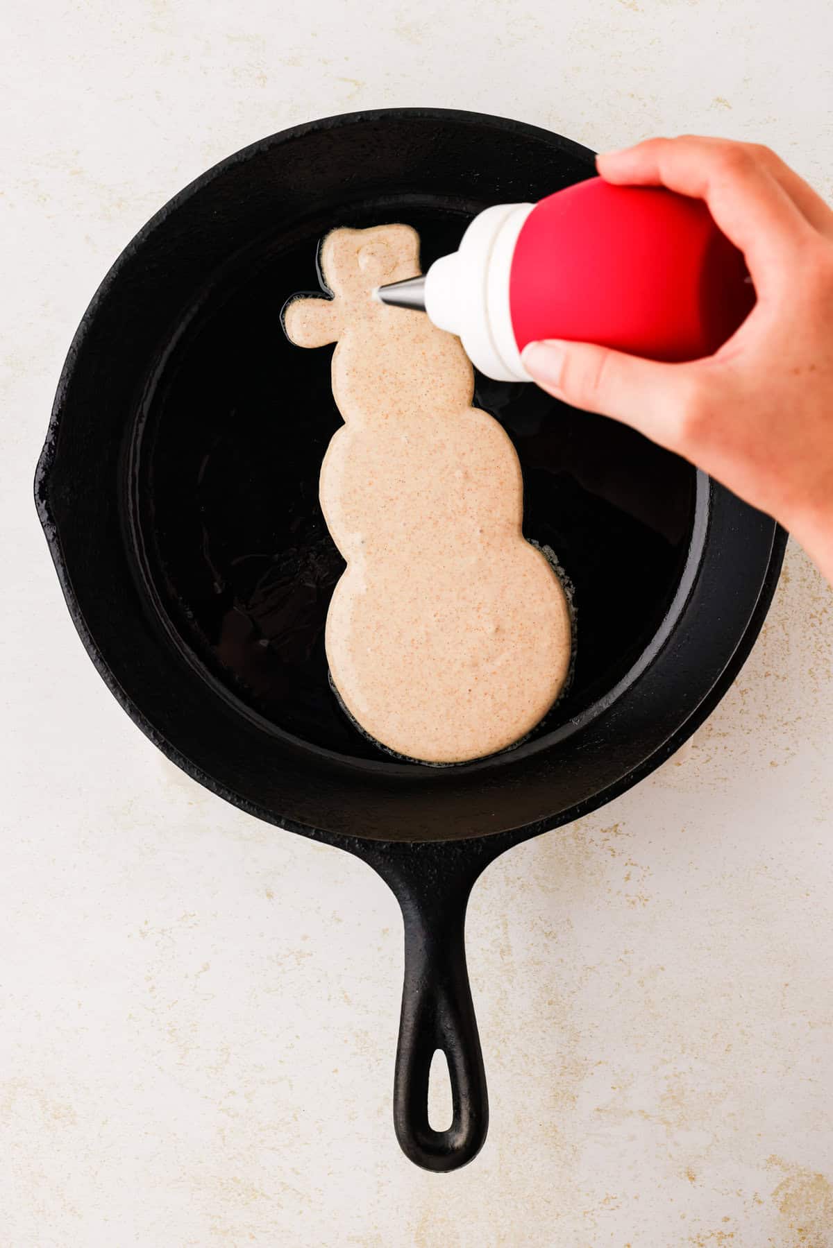 Hand squeezing frosting bulb to fill in the snowmans hat.