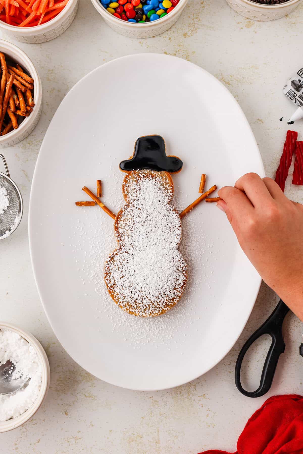 Snowman pancake with pretzel arms being put on it.