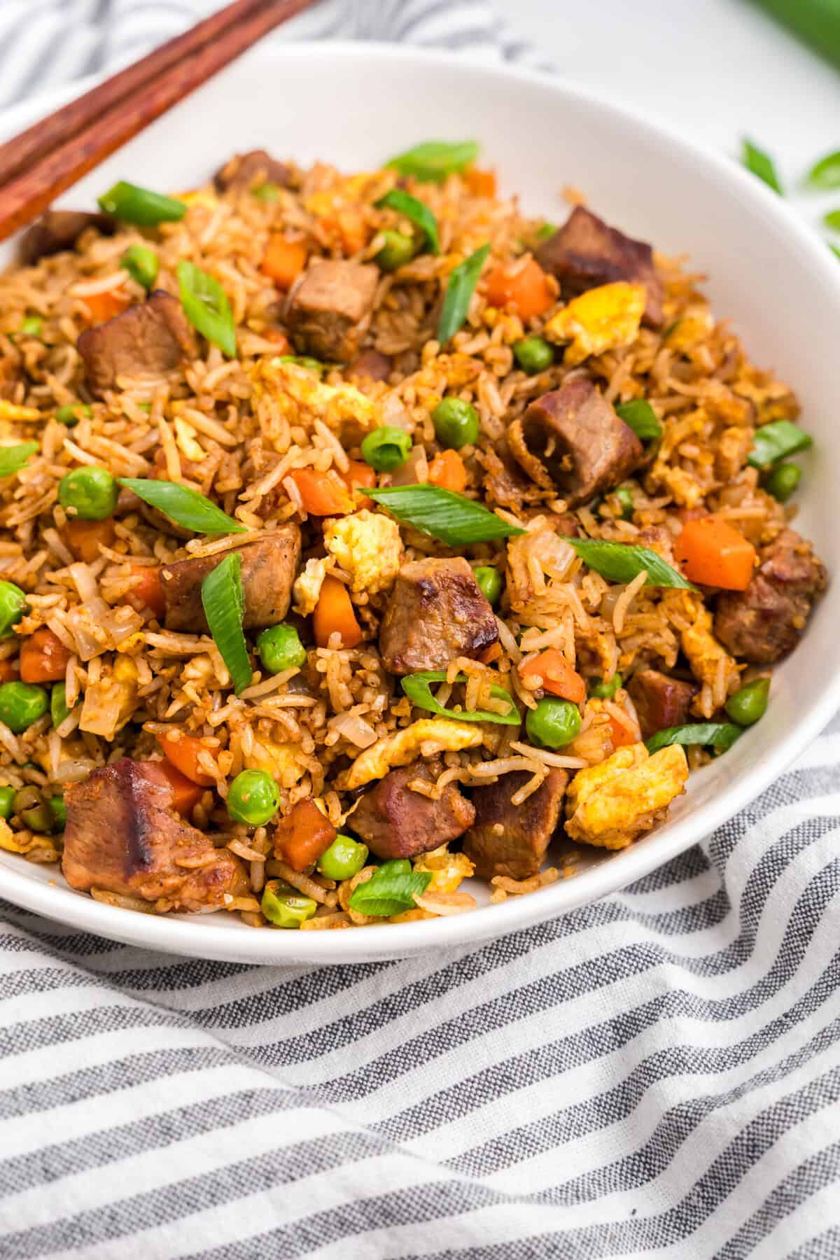 White bowl with steak fried rice in it sitting on a striped towel.