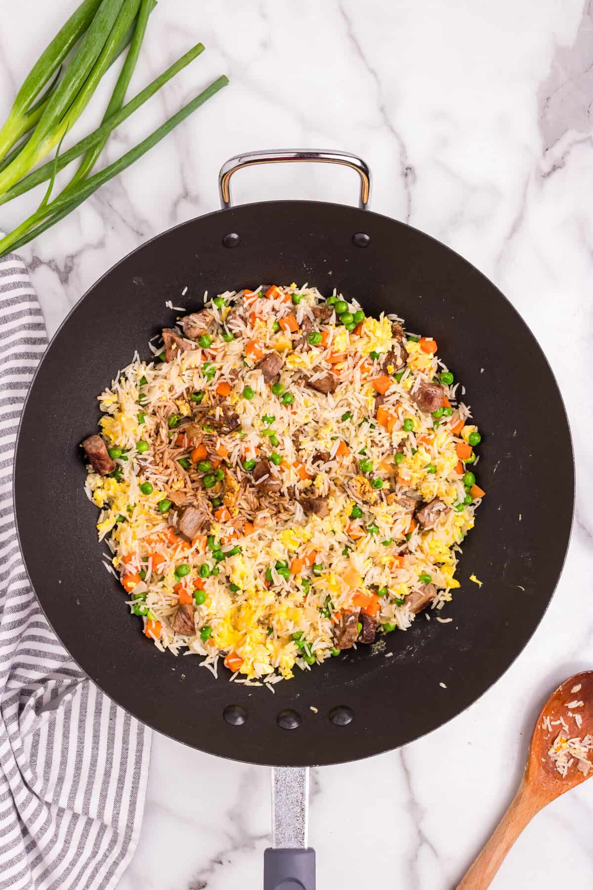 Overhead picture of black skillet pan with uncooked steak fried rice ingredients before oils added.