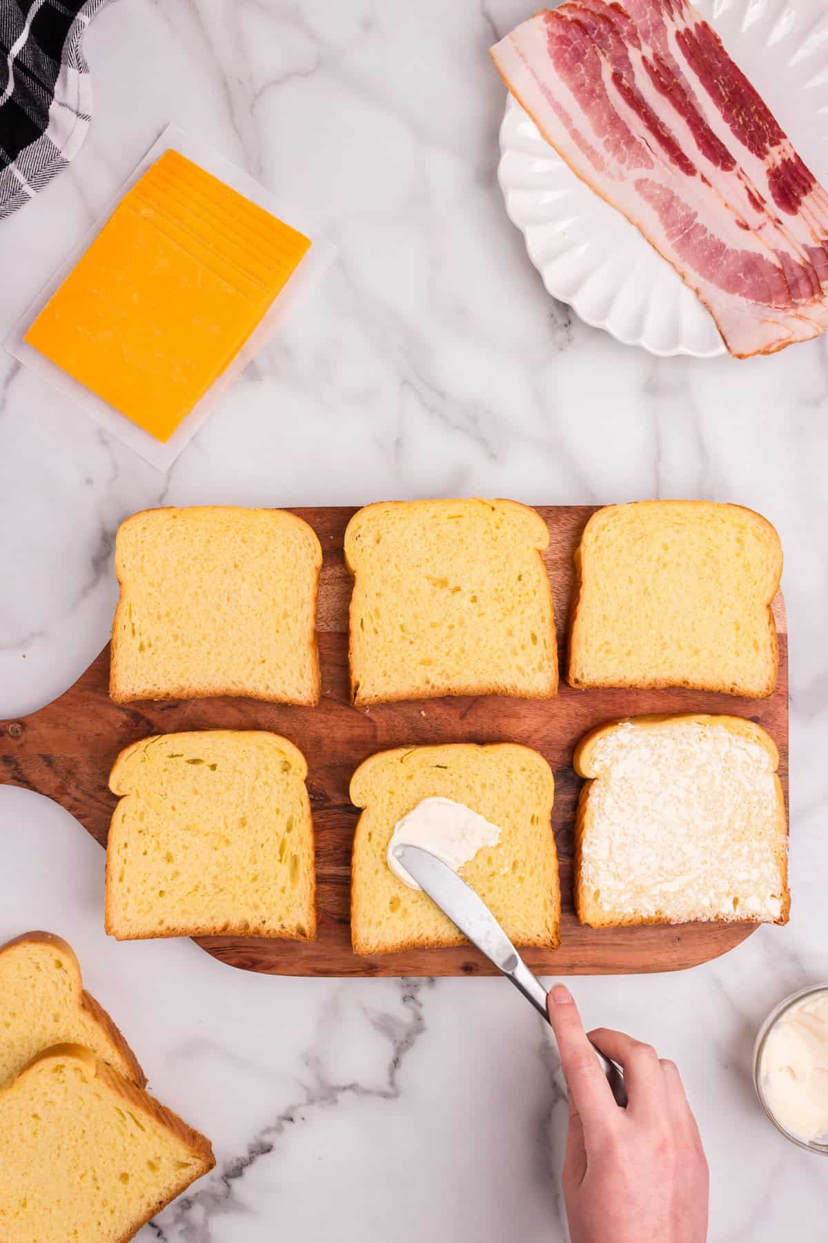 Wooden cutting board with 6 pieces of texas toast with mayonnaise being spread on them.