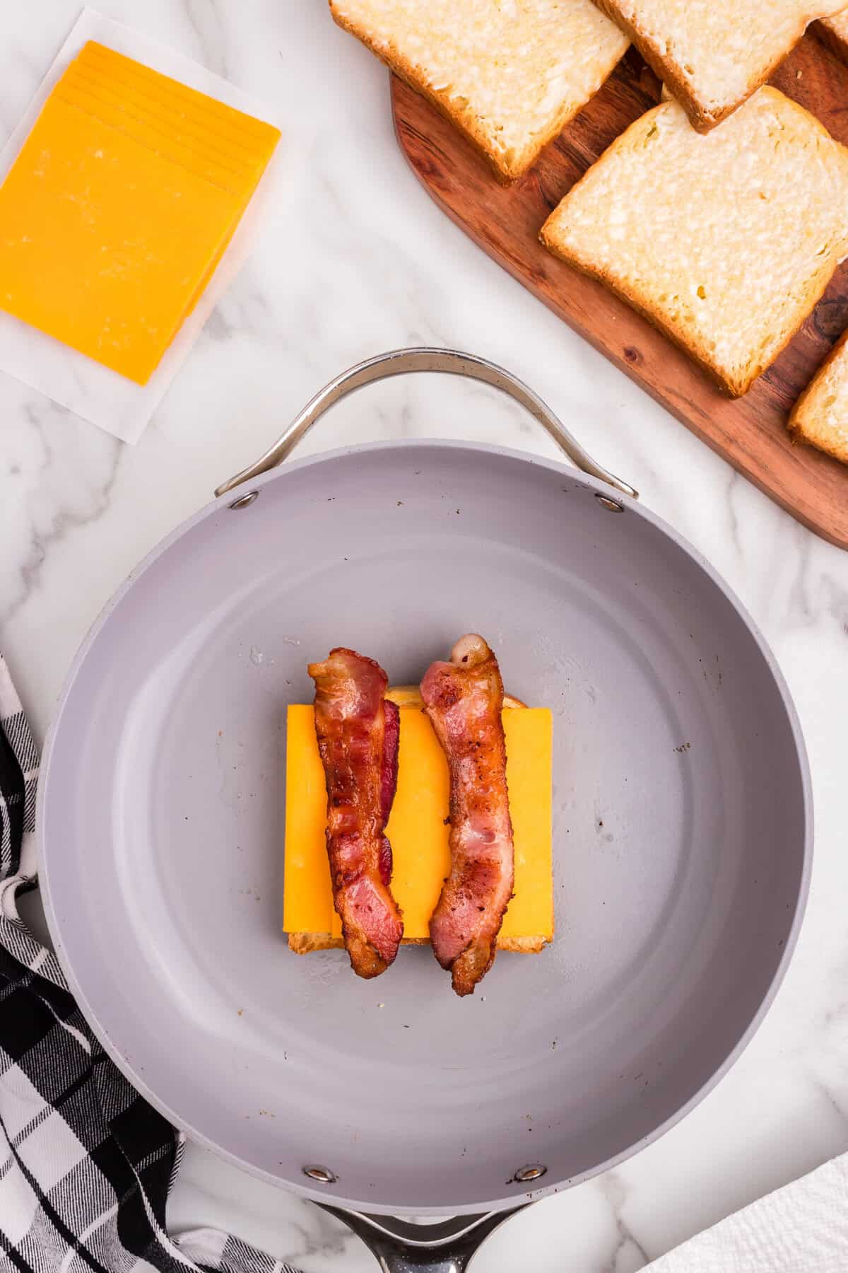 Overhead picture of cheese and 2 pieces of bacon on a frying pan.