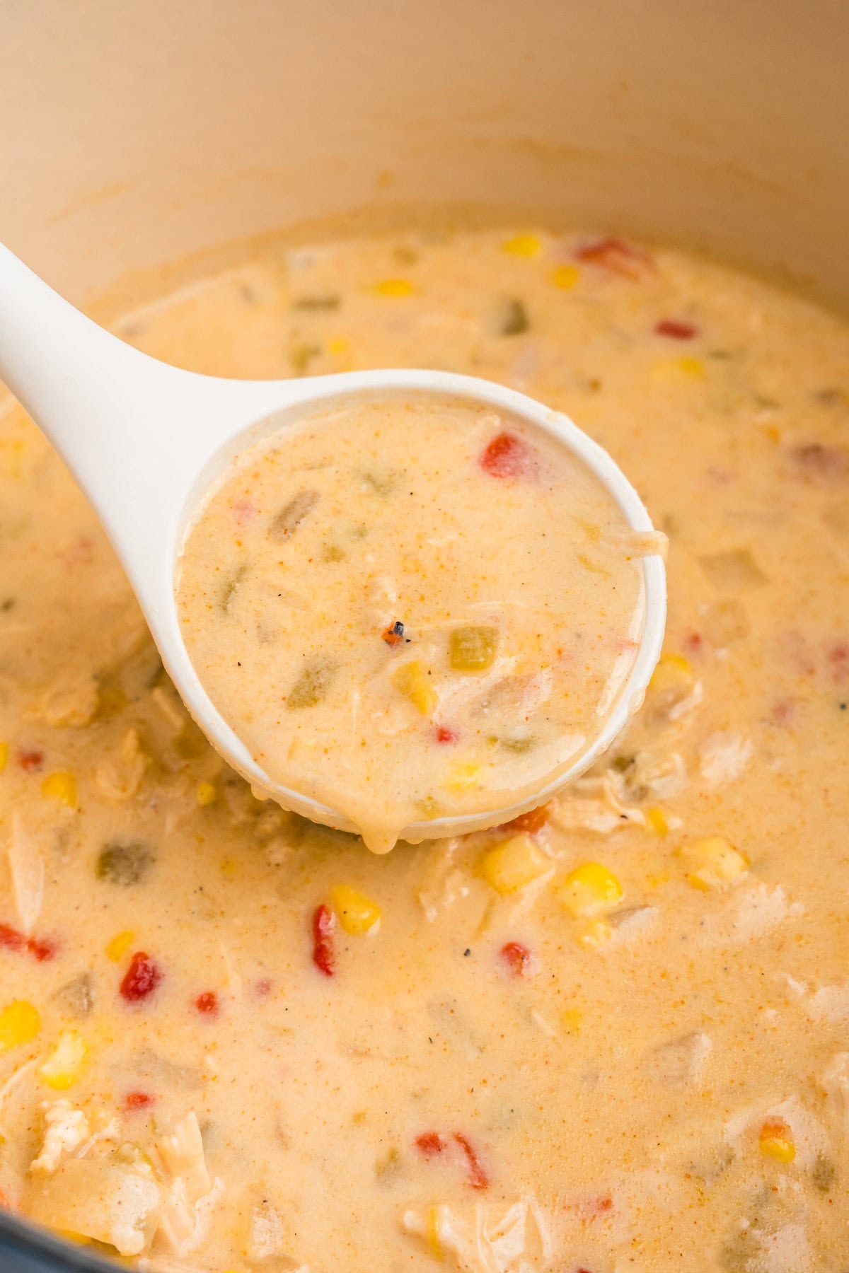 Close up picture of chicken and corn chowder in a pot with a ladle scooping it.