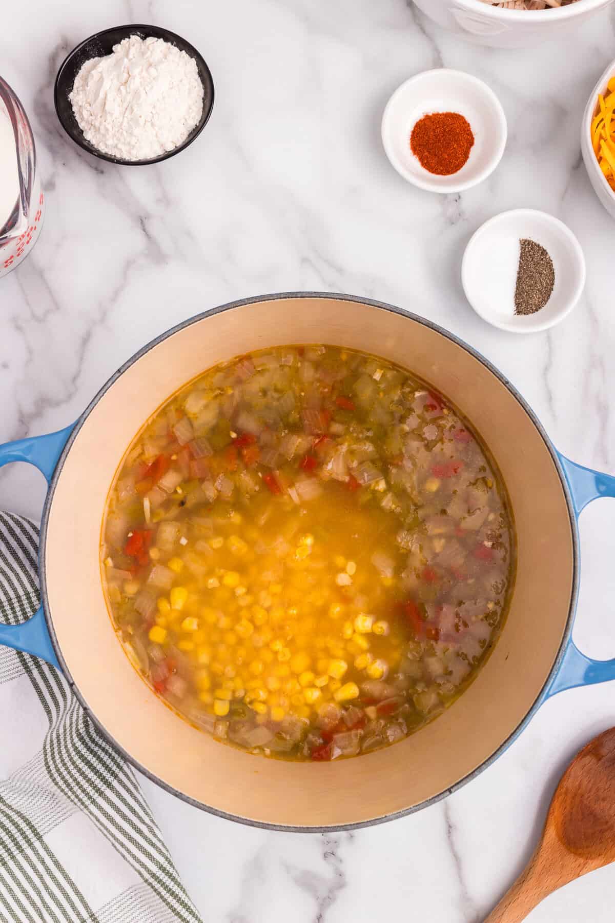 Overhead picture of partially cooked chicken and corn chowder ingredients with added broth and corn.