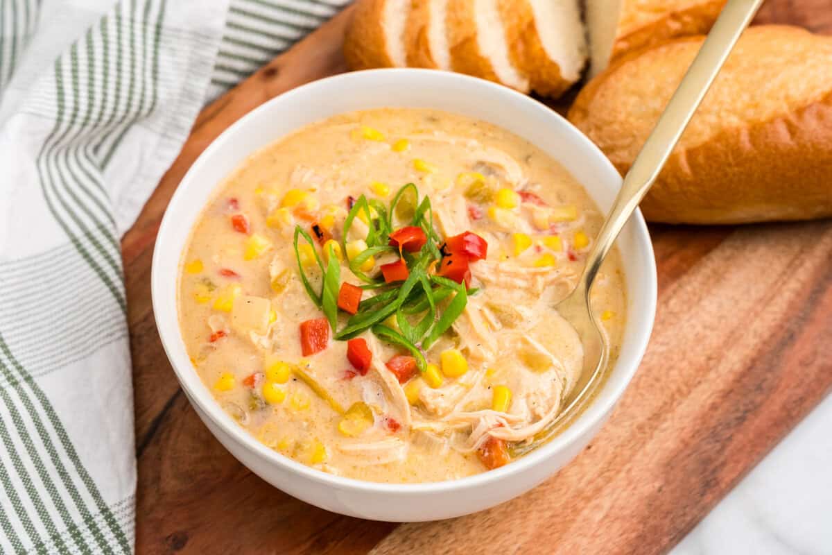 Overhead picture of completed chicken and corn chowder in a bowl on a wooden cutting board.