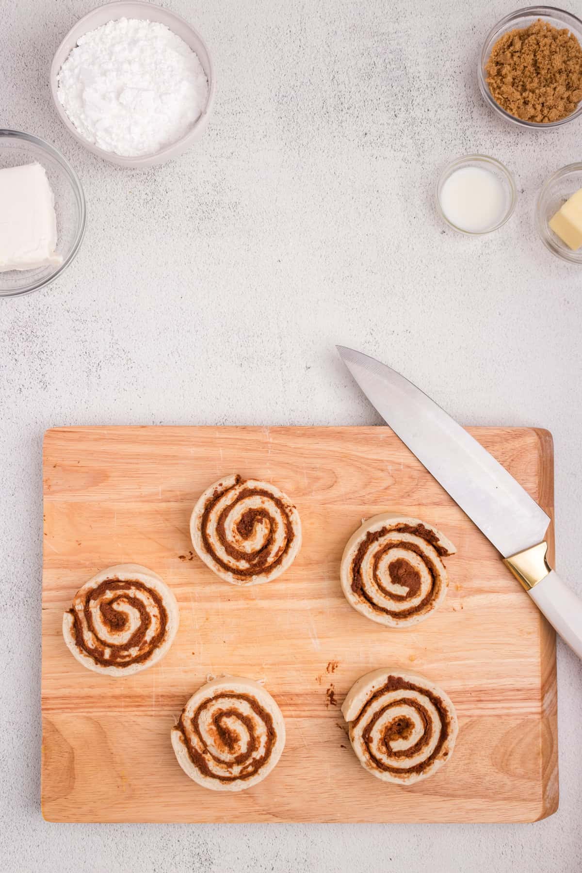 Overhead picture of cinnamon rolls on a wooden cutting board with a knife next to them.