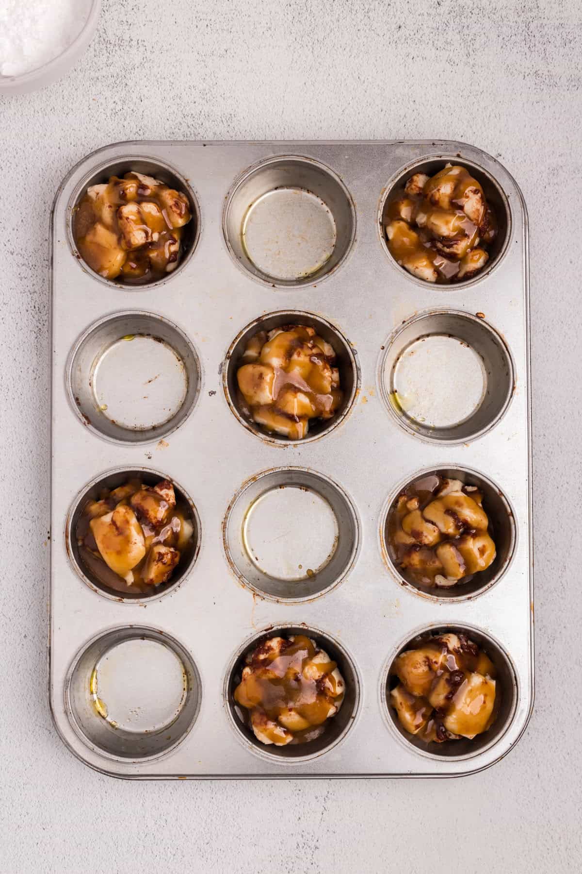 Overhead picture of muffin tin with uncooked cut up cinnamon rolls in it.