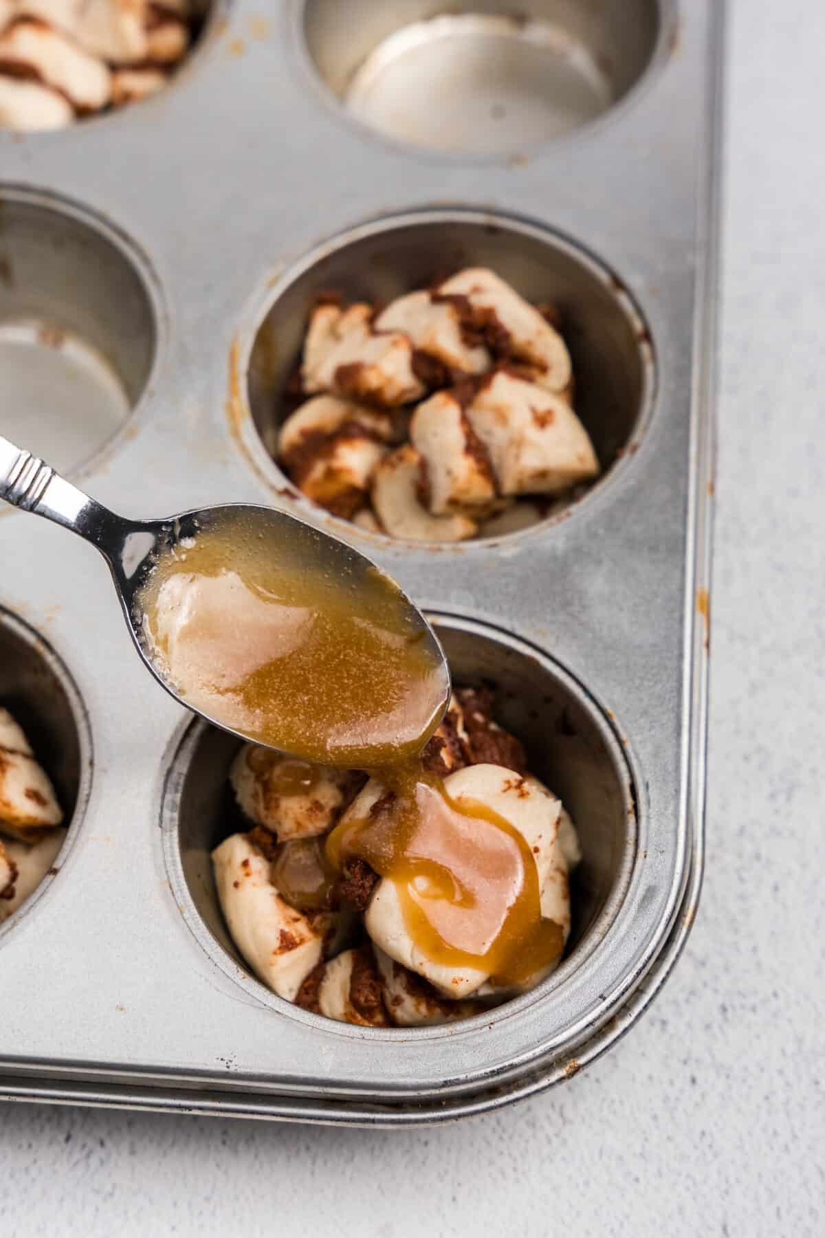 Close up picture of metal spoon pouring brown sugar and powdered sugar mixture over cut up cinnamon rolls.