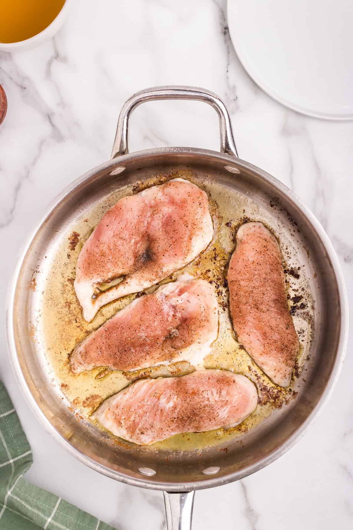 Overhead picture of partially cooked chicken breast in a metal pan.