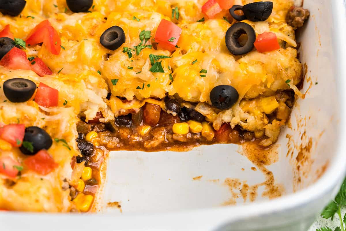 Close up image of white pan with Mexican Tater Tot Casserole in it with a slice taken out.