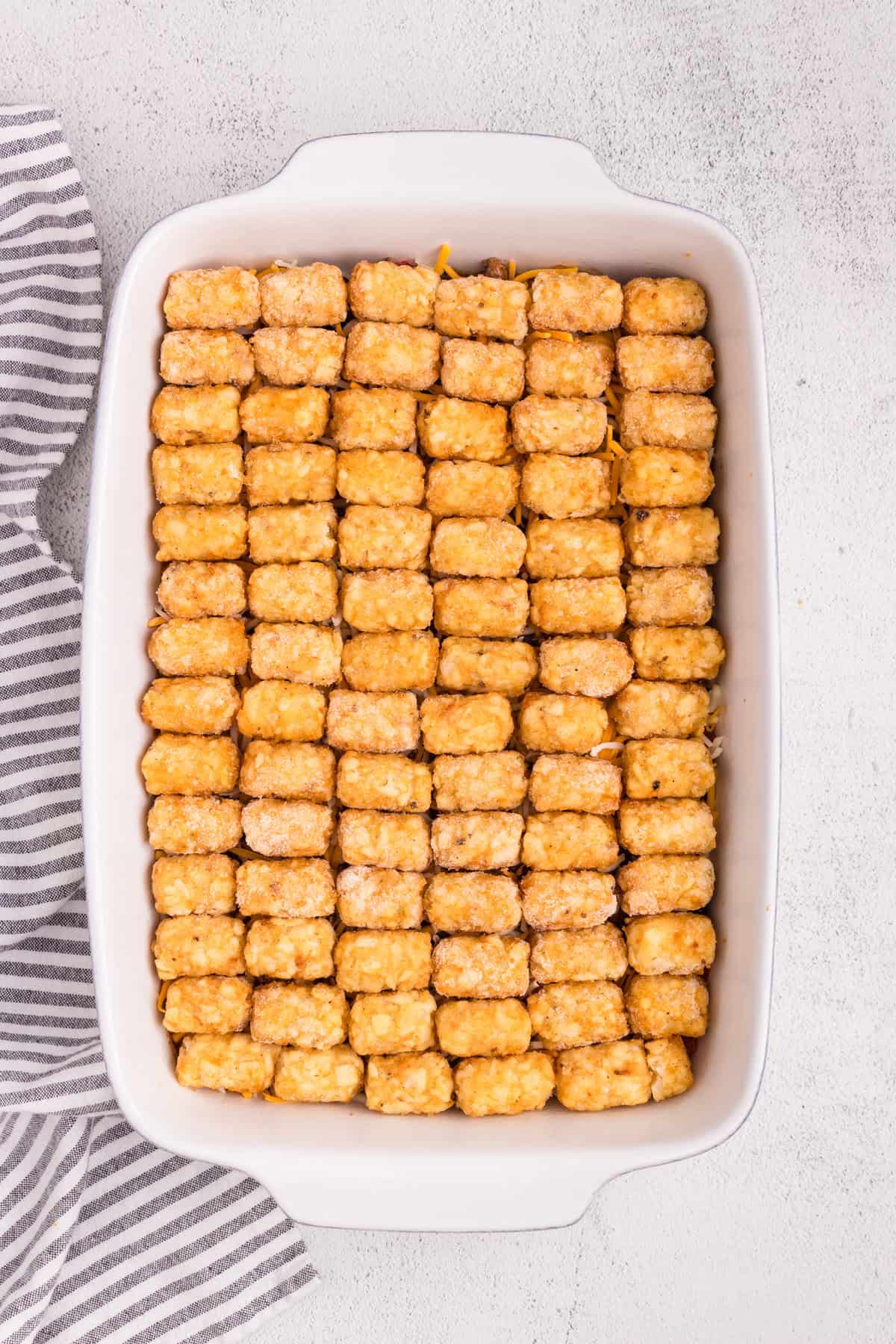 Overhead picture of frozen tater tots lined on top of casserole in a white baking dish.