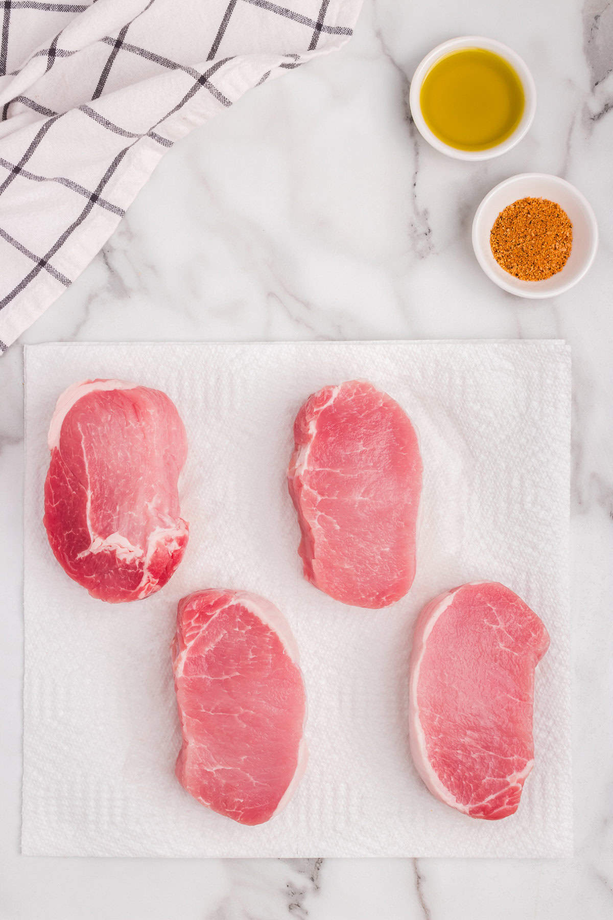 Overhead picture of pork chops laid individually on cutting board with olive oil and pork seasoning next to them.