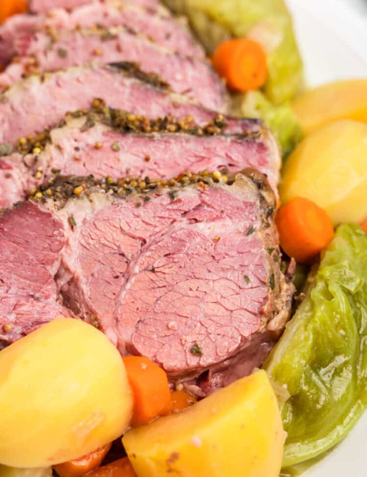 Close up picture of completed corned beef and cabbage and veggies on a white plate.