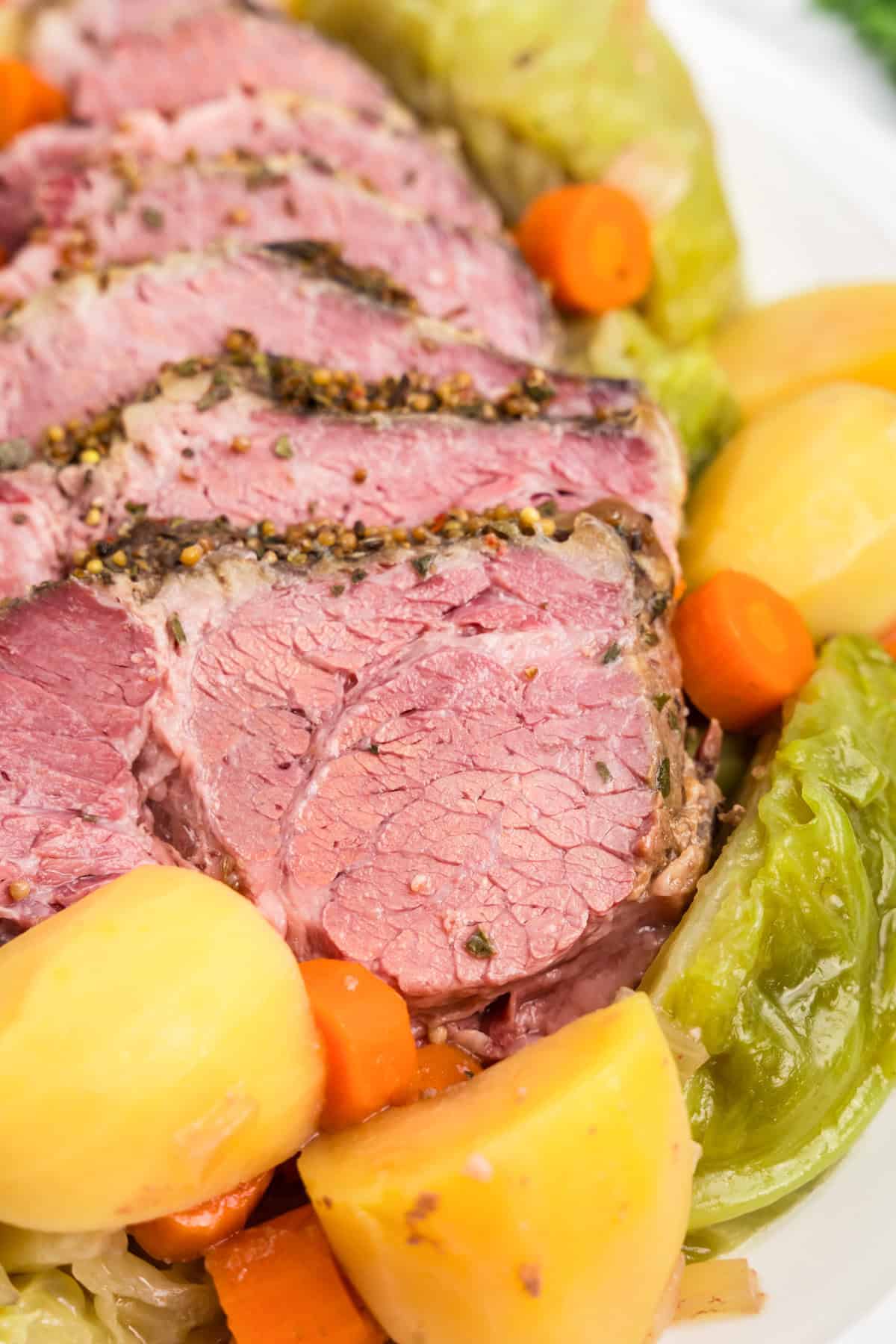 Close up picture of completed corned beef and cabbage and veggies on a white plate.