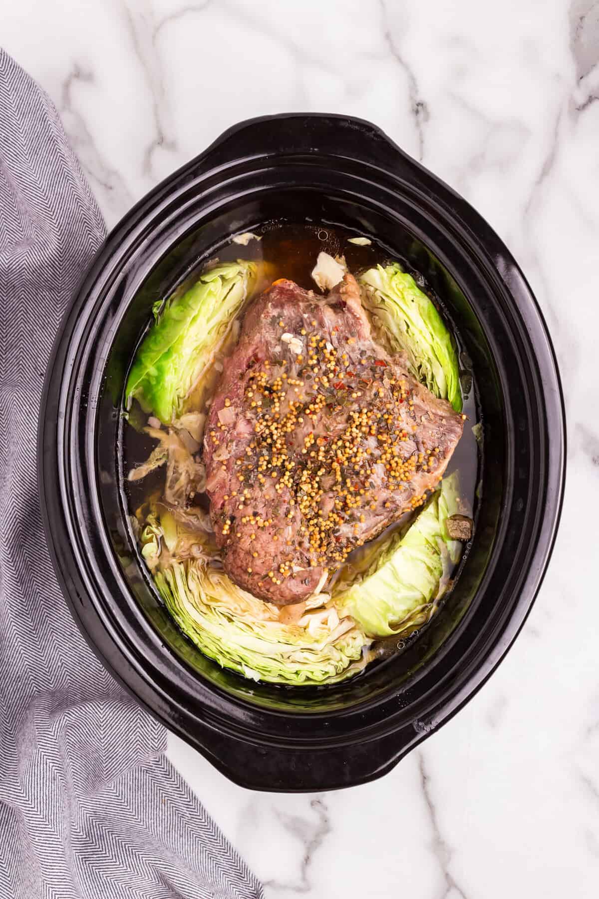 Overhead picture of cooked corned beef with raw cabbage in the crock pot.
