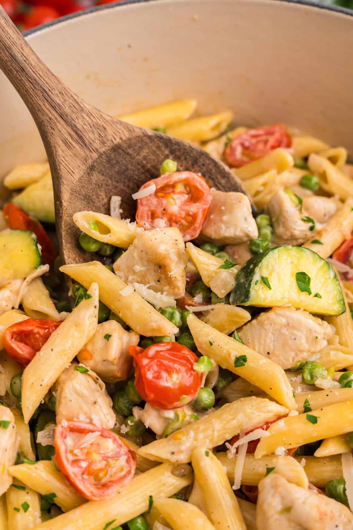 Close up image of a wooden spoon scooping chicken primavera.