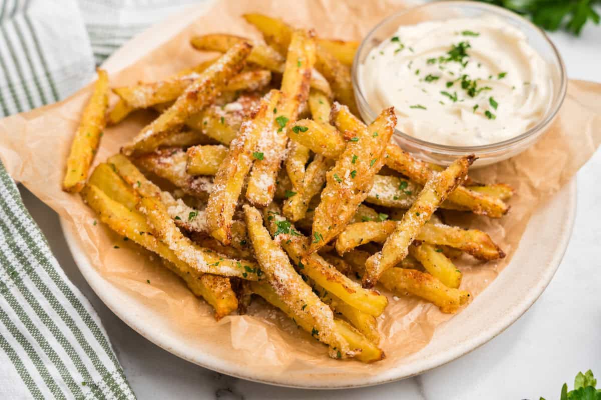 Close up image of completed Garlic Parmesan French Fries and dipping sauce on a white plate.