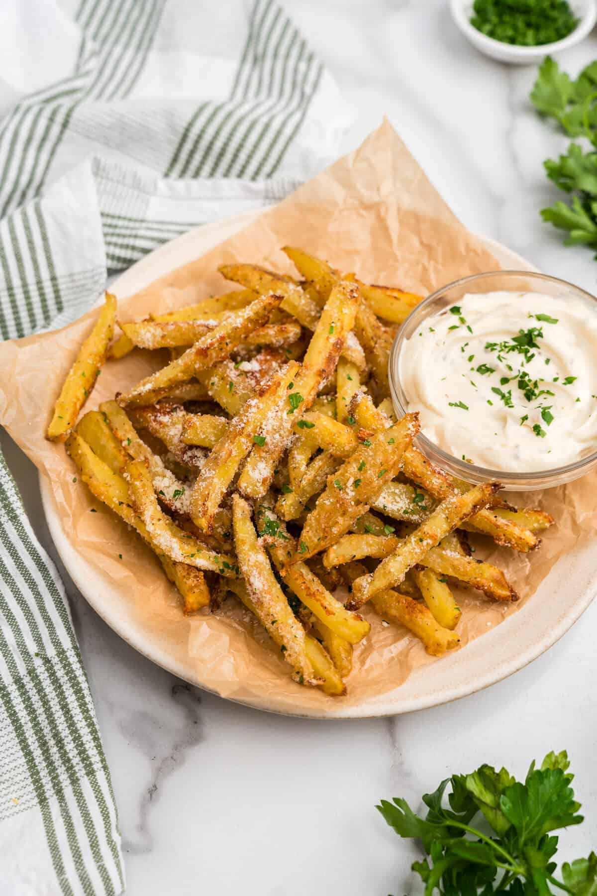 Portrait image of completed garlic parmesan french fries and dipping sauce on a white plate.
