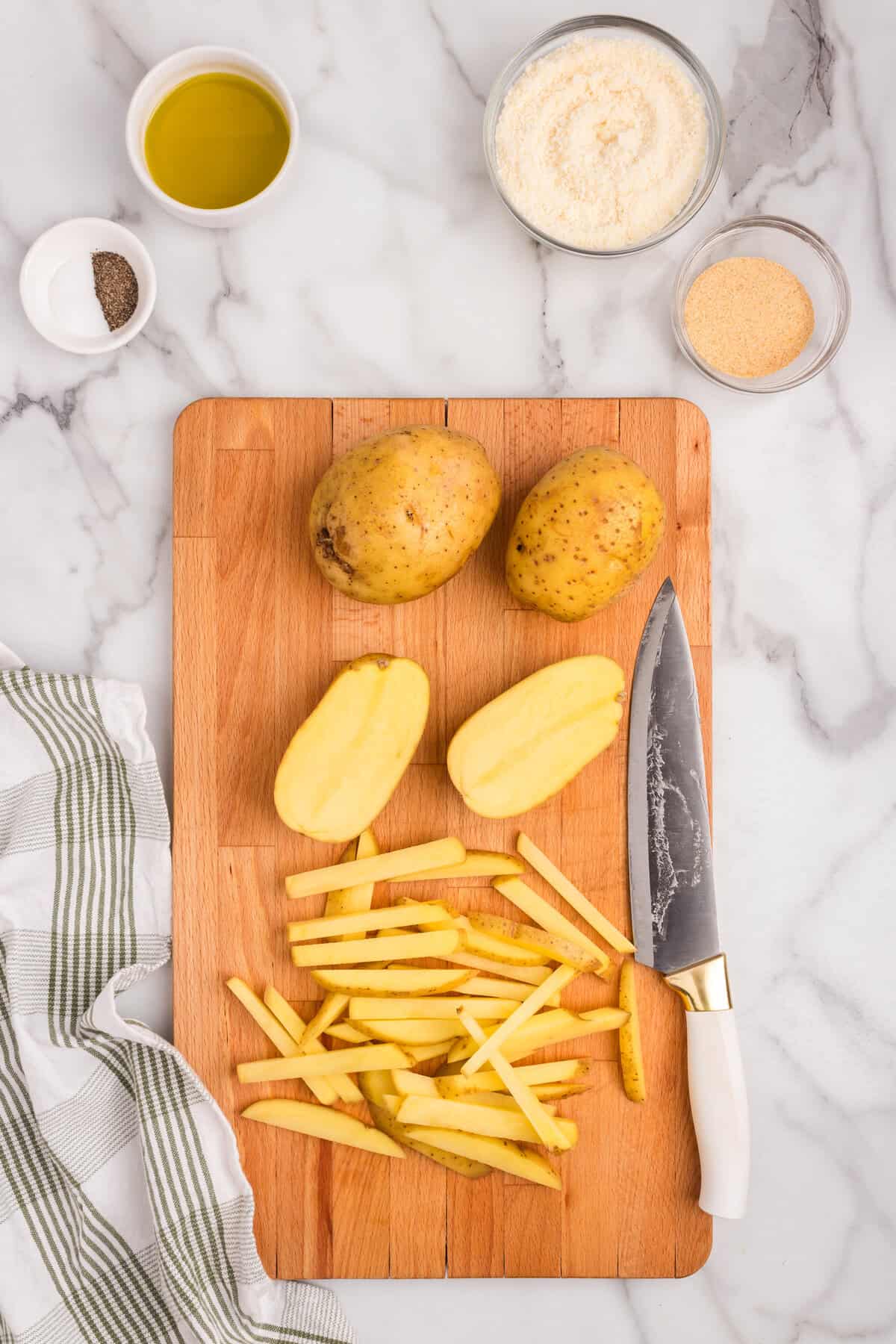 Overhead picture of 2 hole potatoes, 2 halves of potatoes and potatoes cut into fries on a wooden cutting board.