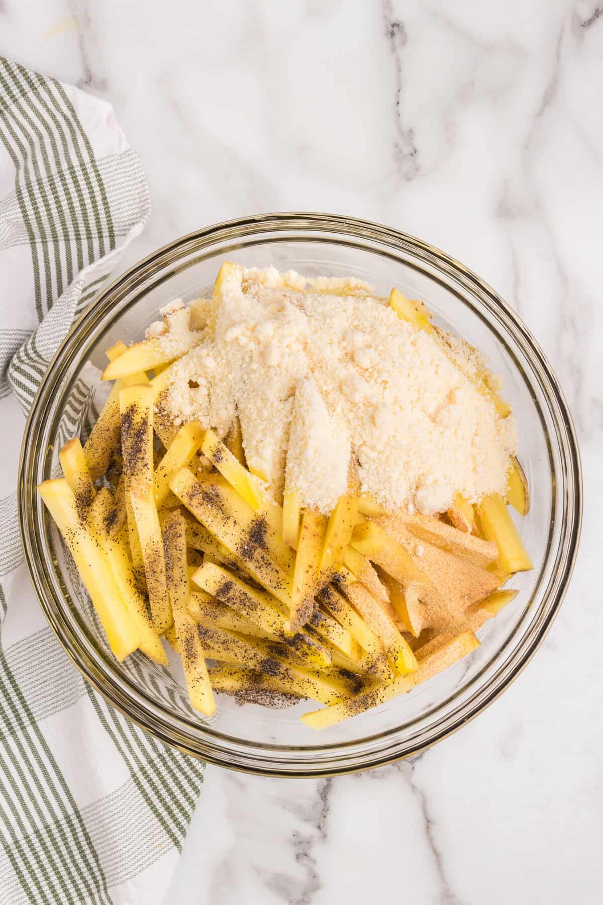 Overhead picture of raw cut potatoes with seasonings on top unmixed.