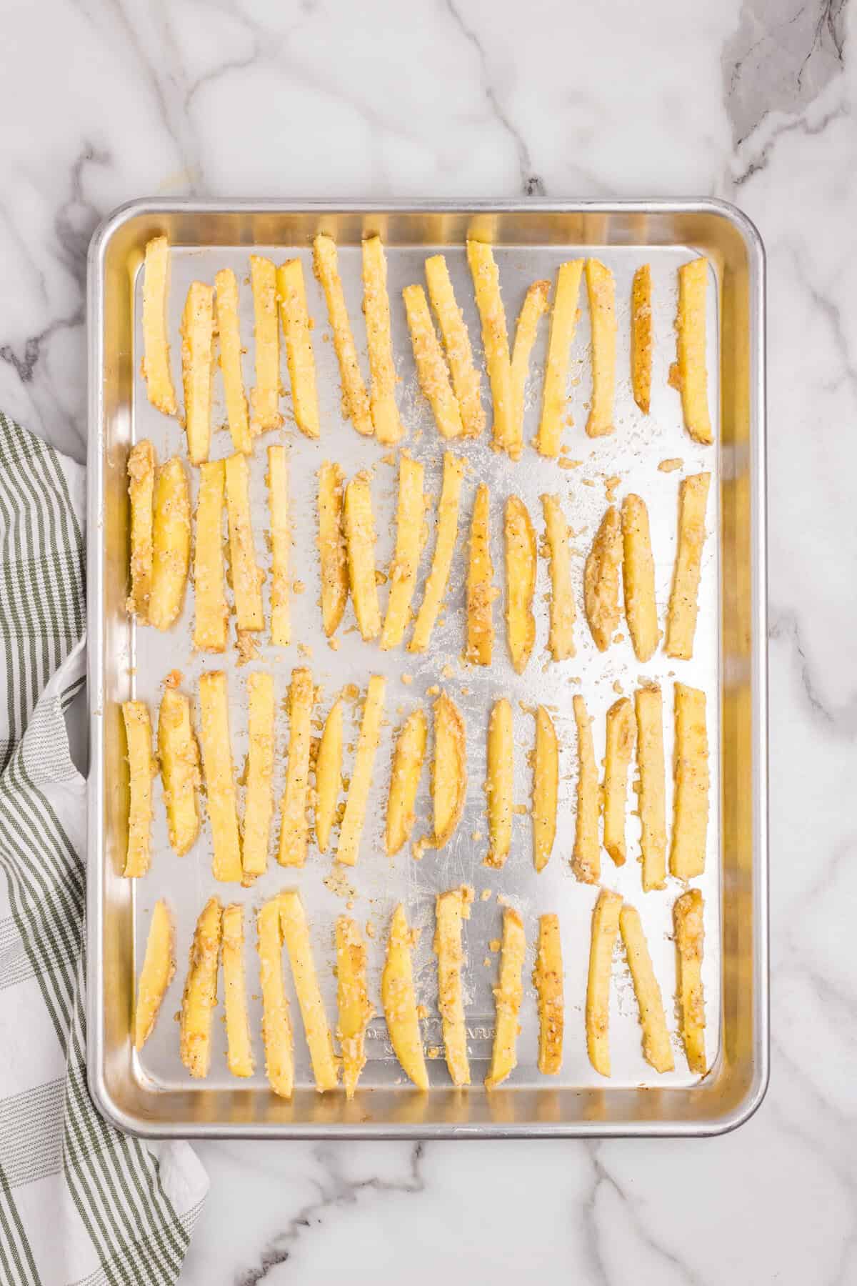 Overhead picture of uncooked seasoned fries spaced out evenly on a baking sheet lined with tin foil.
