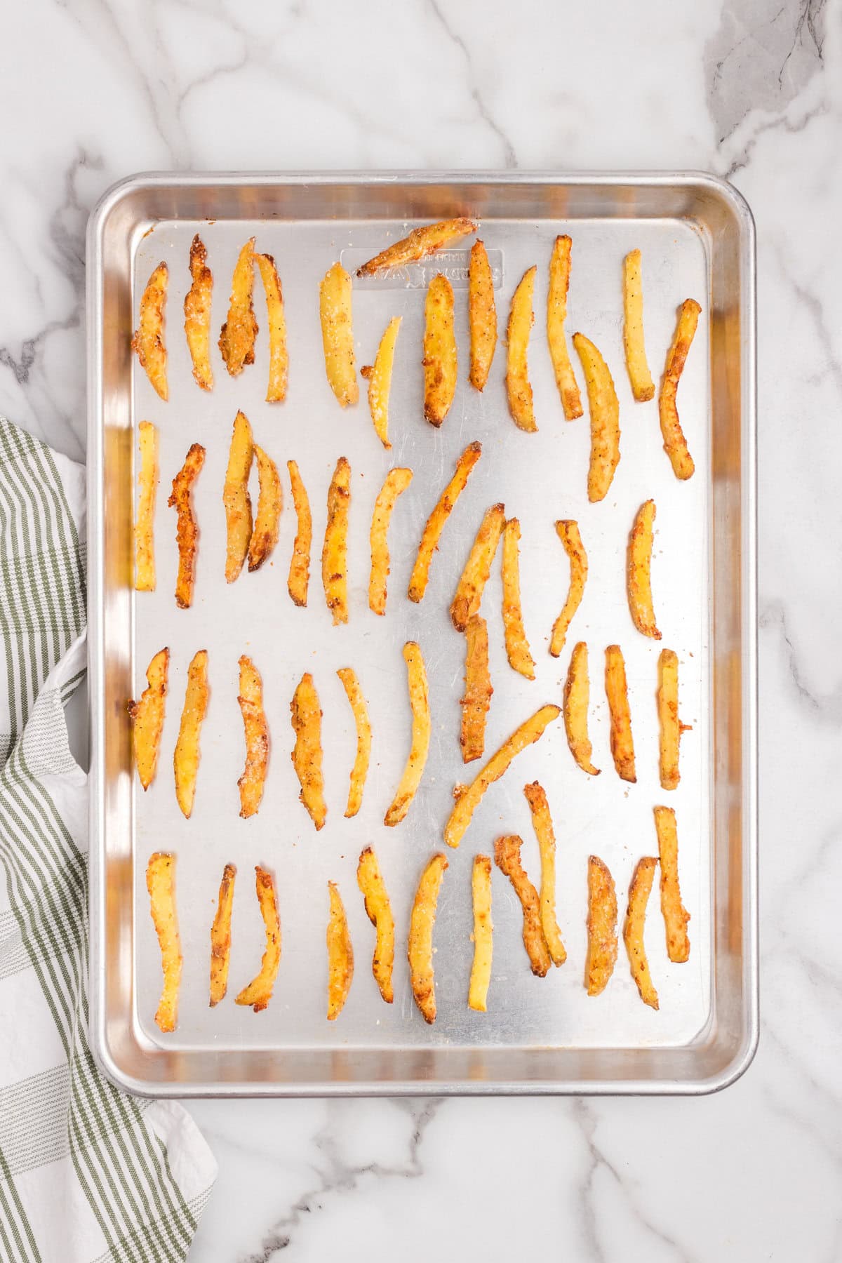 Overhead picture of cooked seasoned fries spaced out evenly on a baking sheet lined with tin foil.