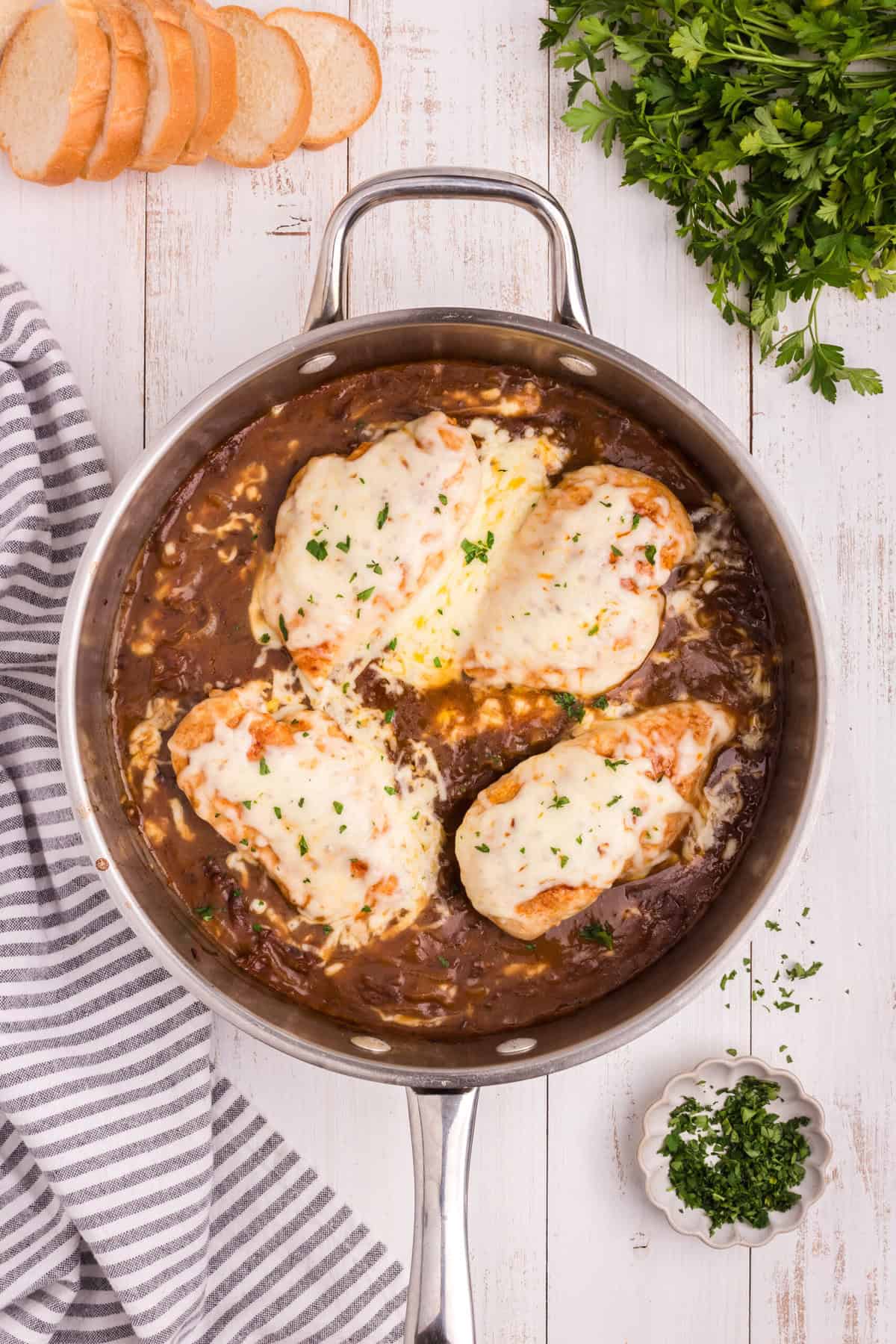 Overhead picture of french onion chicken with melted mozzarella cheese and herbs on top.
